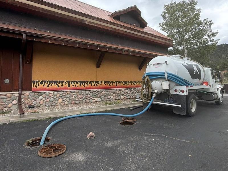 TCS Septic vacuum truck with its hose run across a parking lot to open in-ground access lids at a commercial building